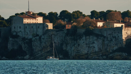 Video - Sailboat floating on calm Mediterranean water in front of the historic Fort Carre in Antibes