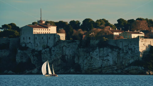 Video - Sailboat floating on calm Mediterranean water in front of the historic Fort Carre in Antibes
