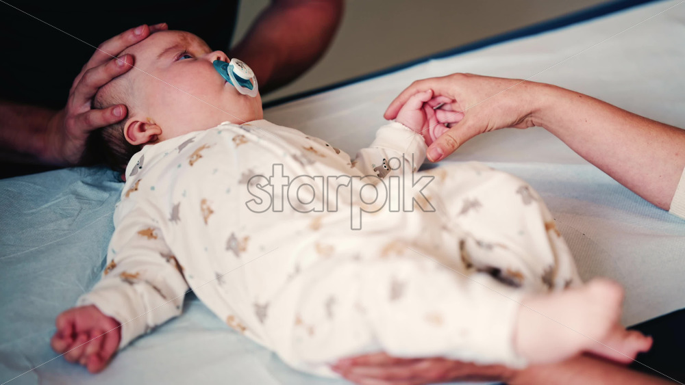 Video - Close up of an adult gently holding a baby's hand while another caregiver supports the infant's head during a medical or wellness check