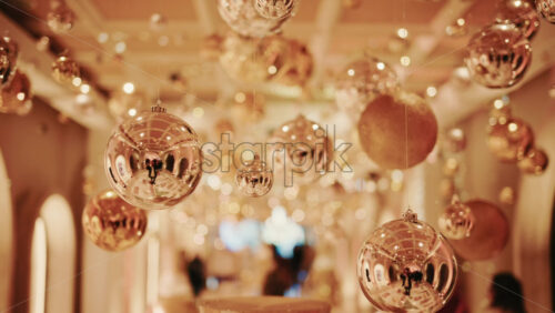 Video - Festive indoor corridor decorated with hanging Christmas ornaments and warm lights. People walking through a seasonal installation during the holiday period