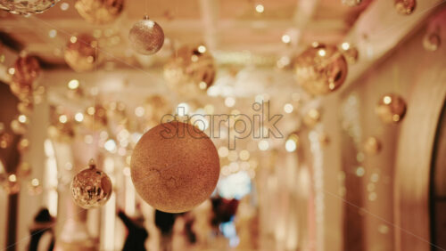 Video - Festive indoor corridor decorated with hanging Christmas ornaments and warm lights. People walking through a seasonal installation during the holiday period