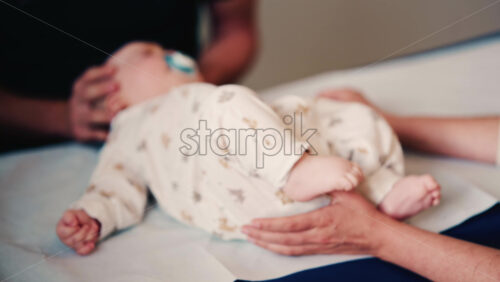 Video - Close up of an adult gently holding a baby's hand while another caregiver supports the infant's head during a medical or wellness check