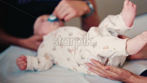 Video - Close up of an adult gently holding a baby's hand while another caregiver supports the infant's head during a medical or wellness check