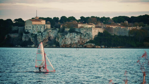 Video - Cannes, France - December 22, 2025: Sailboat floating on calm Mediterranean water in front of the historic Fort Royal