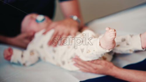 Video - Close up of an adult gently holding a baby's hand while another caregiver supports the infant's head during a medical or wellness check
