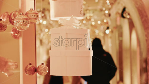 Video - Minimal white gift box suspended among golden Christmas ornaments and warm fairy lights in an indoor festive corridor