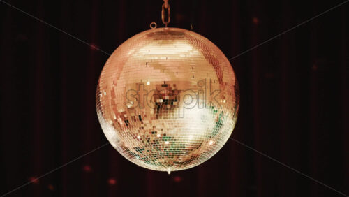 Video - Close up of a golden mirrored disco ball hanging against a dark background, reflecting soft light