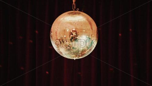 Video - Close up of a golden mirrored disco ball hanging against a dark background, reflecting soft light