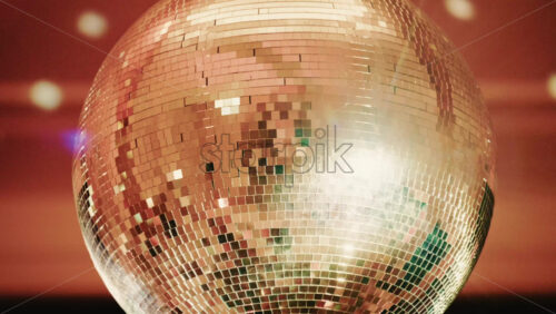 Video - Close up of a shiny disco ball reflecting light patterns in a warmly lit interior environment