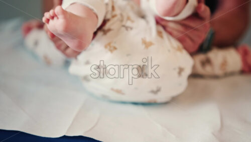 Video - Close up of an infant's legs and feet while caregivers gently reposition the baby during a care or examination session
