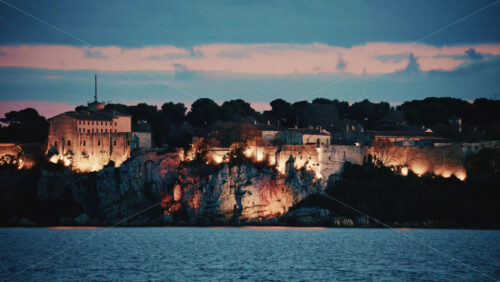 Video - Scenic view of a historic coastal fortress illuminated at dusk, overlooking the sea