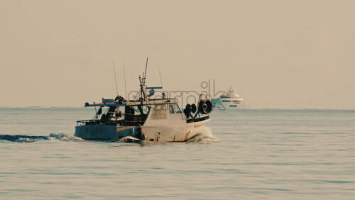 Video - Antibes, France - December 22, 2025: Small fishing boat navigating calm Mediterranean waters off the coast of France, with a luxury yacht visible in the background