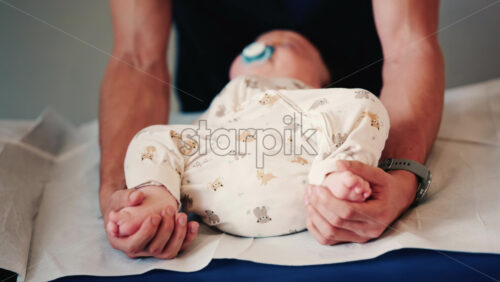 Video - Close up of an infant's legs and feet while caregivers gently reposition the baby during a care or examination session