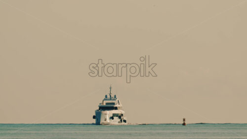 Video - Front view of a luxury motor yacht cruising slowly across calm Mediterranean waters, with a navigation buoy visible nearby