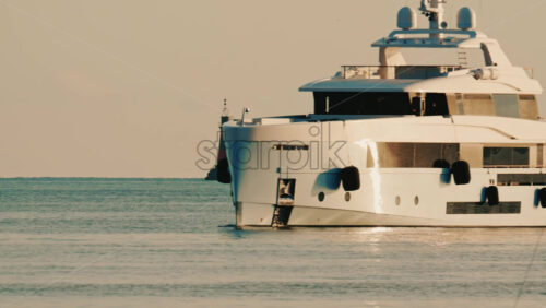 Video - Side view of a modern luxury yacht moving across calm sea water with a lighthouse in the distance