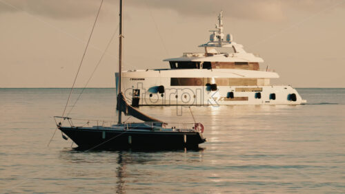 Video - Luxury motor yacht anchored on calm Mediterranean waters near the French Riviera, with a smaller sailboat in the foreground