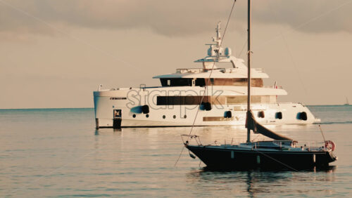 Video - Luxury motor yacht anchored on calm Mediterranean waters near the French Riviera, with a smaller sailboat in the foreground