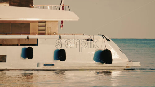 Video - Side view of a modern luxury yacht moving across calm sea water with a lighthouse in the distance