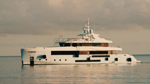 Video - Side view of a modern luxury yacht moving across calm sea water with a lighthouse in the distance
