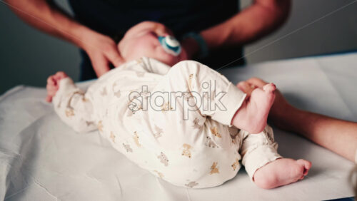 Video - Close up of an infant's legs and feet while caregivers gently reposition the baby during a care or examination session
