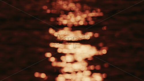 Video - Close up of orange and gold sunset reflections moving across gentle water ripples