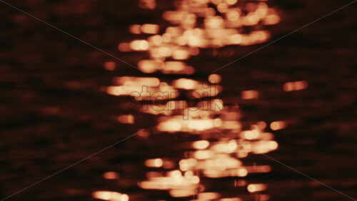 Video - Close up of orange and gold sunset reflections moving across gentle water ripples