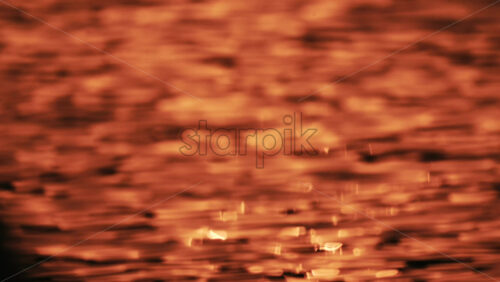 Video - Close up of orange and gold sunset reflections moving across gentle water ripples