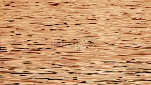 Video - Close up of orange and gold sunset reflections moving across gentle water ripples