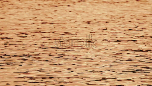 Video - Close up of orange and gold sunset reflections moving across gentle water ripples