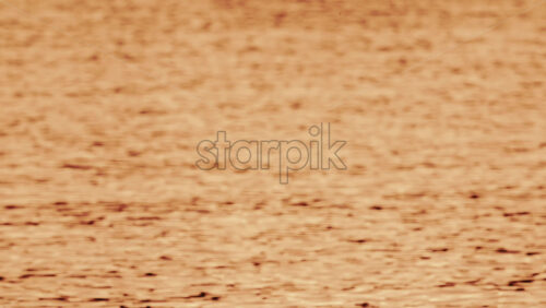 Video - Close up of orange and gold sunset reflections moving across gentle water ripples