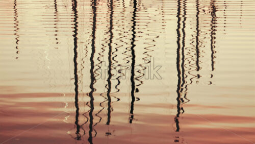 Video - Reflections of boat masts distorted on still marina water during sunset