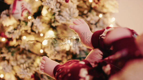 Video - Close up of baby feet wearing festive pajamas held in front of a softly lit Christmas tree