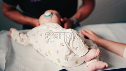 Video - Close up of an infant's legs and feet while caregivers gently reposition the baby during a care or examination session