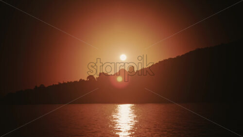 Video - Sun setting behind coastal hills with golden light reflecting on calm water in the French Riviera