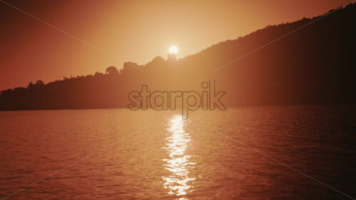 Video - Sun setting behind coastal hills with golden light reflecting on calm water in the French Riviera