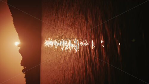 Video - Sun setting behind coastal hills with golden light reflecting on calm water in the French Riviera. Vertical