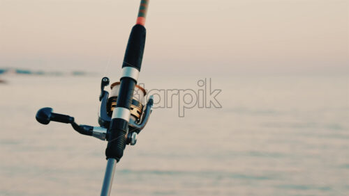 Video - Close up of a fishing rod and reel positioned near the sea, with a blurred boat in the background