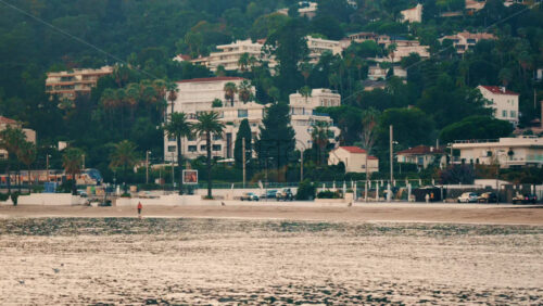 Video - Golfe Juan, France - December 22, 2025: Coastal trains traveling parallel to the shoreline, with palm trees, beachfront, and hillside residential buildings in the background
