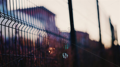 Video - Close up of a metal fence with softly blurred lights of a train passing in the background at dusk