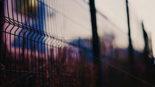 Video - Close up of a metal fence with softly blurred lights of a train passing in the background at dusk