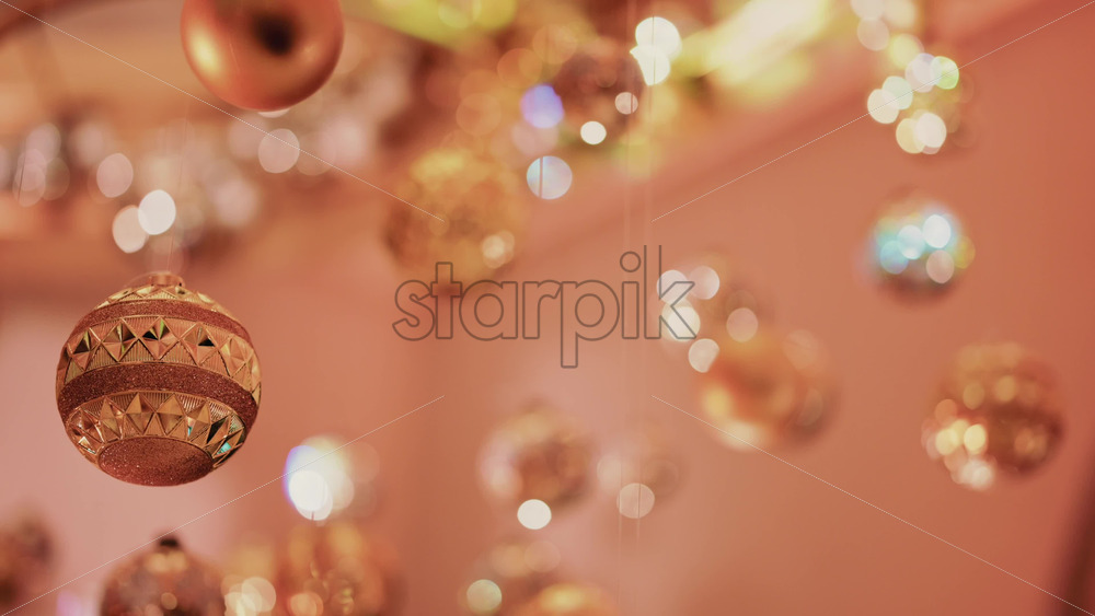 Video - Multiple golden Christmas ornaments hanging beneath a decorative indoor installation