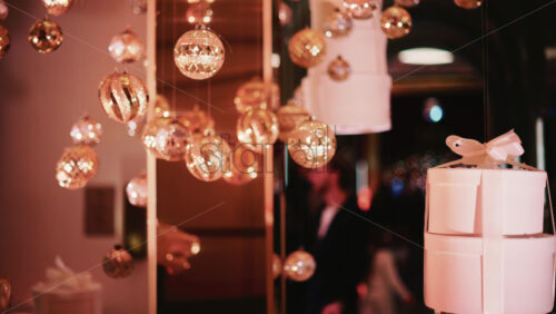 Video - Golden Christmas baubles hanging from a structure alongside a suspended white gift box, with people blurred in the background
