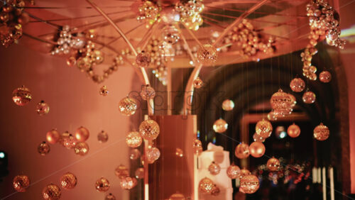 Video - Golden Christmas baubles hanging from a structure alongside a suspended white gift box, with people blurred in the background