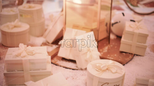 Video - Close up of white, ribbon wrapped gift boxes arranged on a snowy decorative surface, with warm ambient lighting and festive props in the background