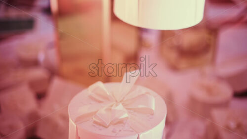 Video - Detail shot of a round white gift box topped with a satin ribbon, surrounded by softly blurred festive decor and warm lights