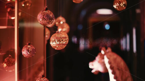 Video - Golden Christmas baubles hanging from a structure alongside a suspended white gift box, with people blurred in the background