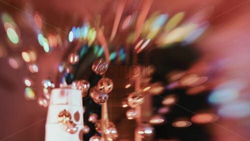 Video - Golden Christmas baubles hanging from a structure alongside a suspended white gift box, with people blurred in the background