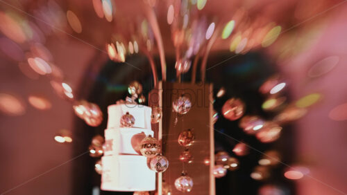 Video - Golden Christmas baubles hanging from a structure alongside a suspended white gift box, with people blurred in the background