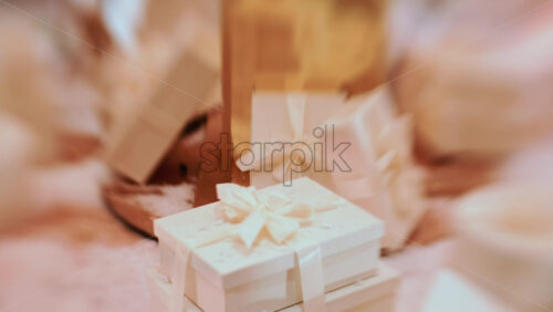 Video - Close up of white, ribbon wrapped gift boxes arranged on a snowy decorative surface, with warm ambient lighting and festive props in the background