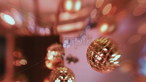 Video - Close up of a single golden Christmas ornament suspended in the air, sharply focused against a softly lit festive background